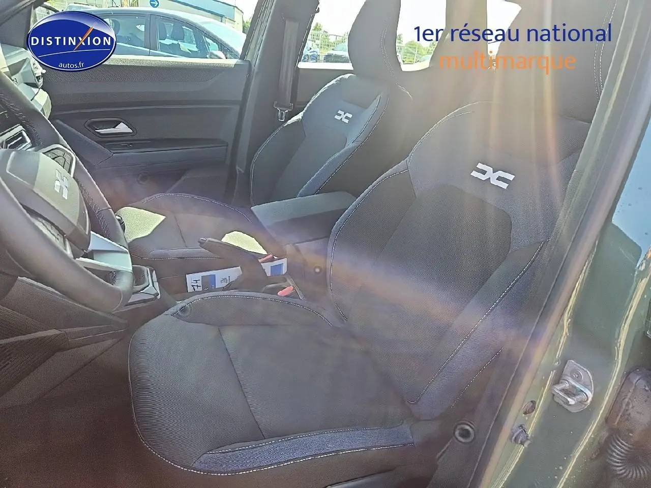 Vue intérieure côté conducteur du Dacia Duster vert kaki 2025, sièges tissu avec logo DC brodé et accoudoir central.