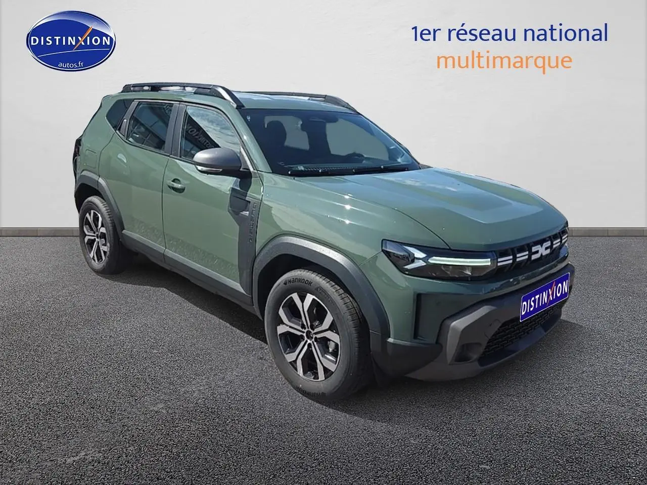 Vue 3/4 avant droit du Dacia Duster 2025 vert kaki avec jantes alu et barres de toit visibles.