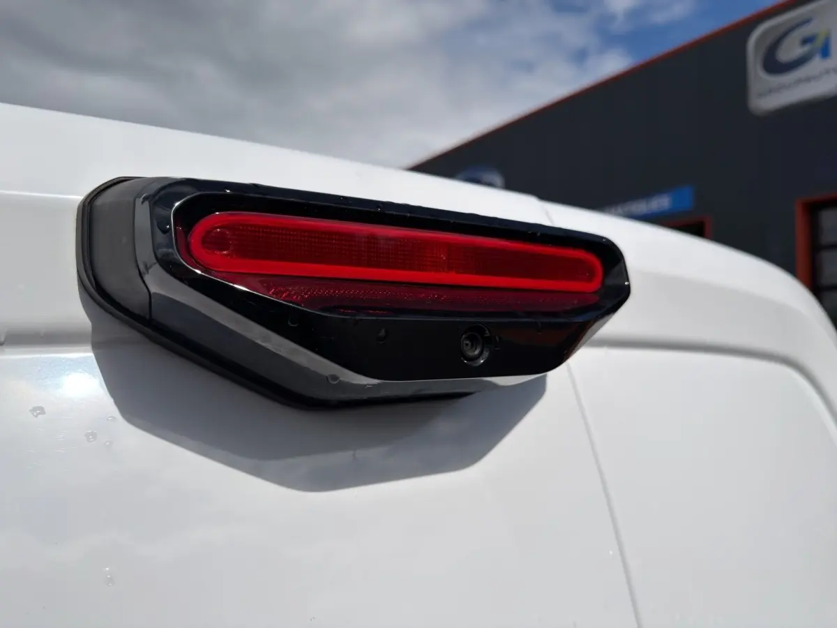 Gros plan sur le feu arrière droit noir et rouge du Citroën Berlingo blanc, vue en légère contre-plongée.