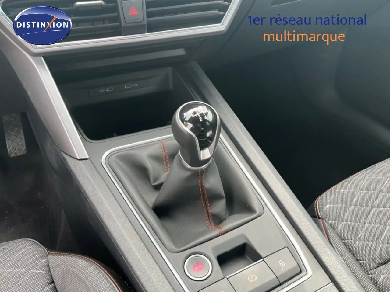 Gros plan sur la console centrale et levier de vitesses manuel du SEAT LEON ST gris métallique, intérieur tissu noir avec surpiqûres rouges.