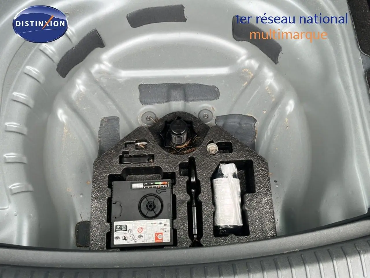 Vue plongeante sur le coffre ouvert d'une SEAT LEON ST gris magnétique, montrant le rangement pour roue de secours et outils.