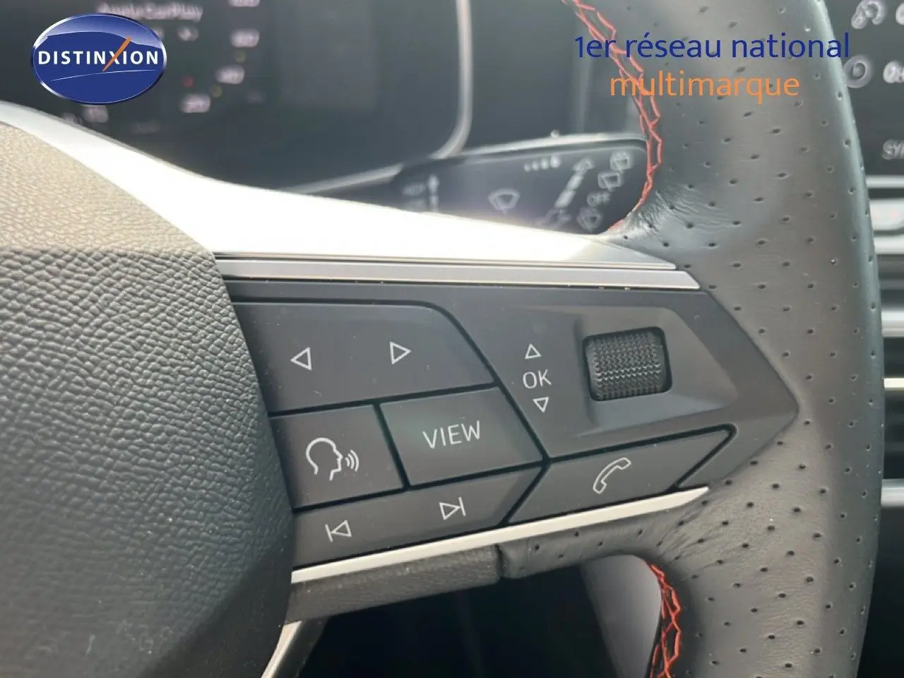 Gros plan sur les commandes multifonctions à droite du volant perforé avec surpiqûres rouges du SEAT LEON ST gris magnétique.