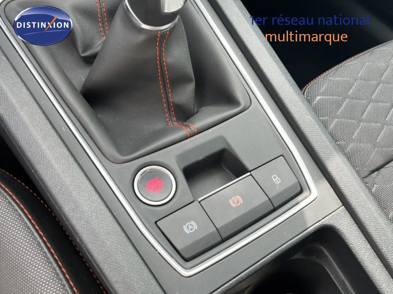 Gros plan sur la console centrale avec levier de vitesse et boutons de commande, intérieur gris noir avec surpiqûres rouges.