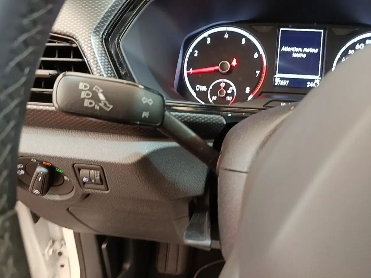 Vue intérieure du tableau de bord du Volkswagen T-Cross blanc, avec compteur et commandes au volant visibles.