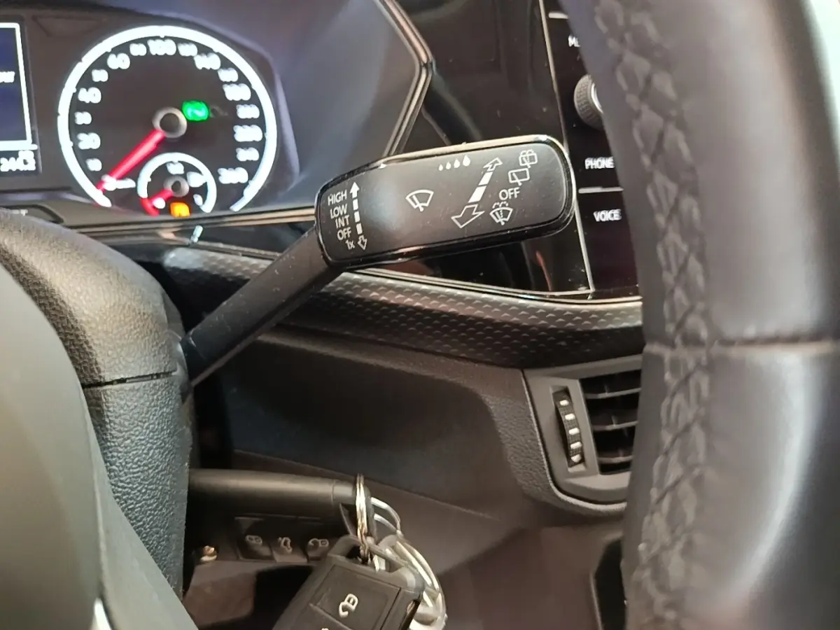 Gros plan sur la manette d’essuie-glace à gauche du volant cuir du Volkswagen T-Cross blanc, tableau de bord en arrière-plan.