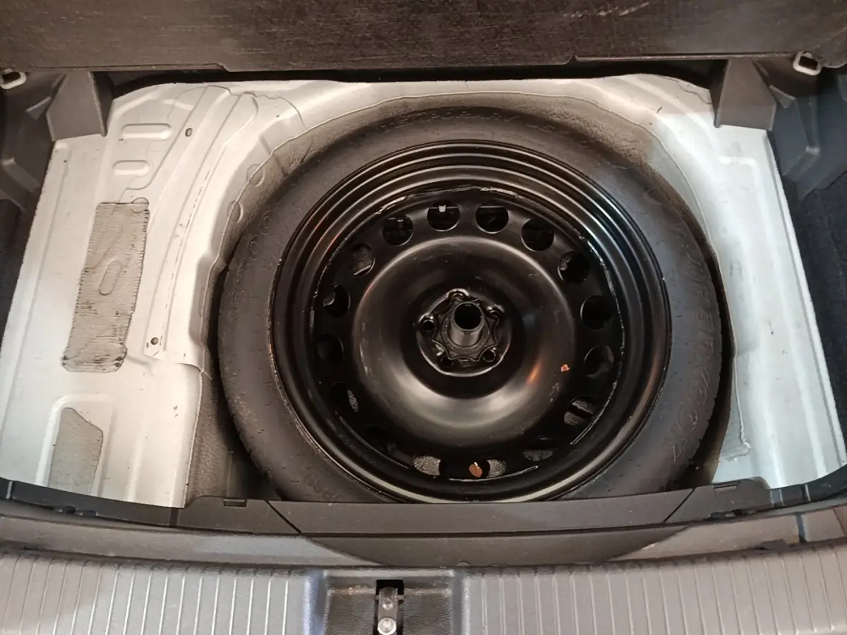 Roue de secours galette noire dans le coffre d’un Volkswagen T-Cross blanc, vue plongeante sur le compartiment.