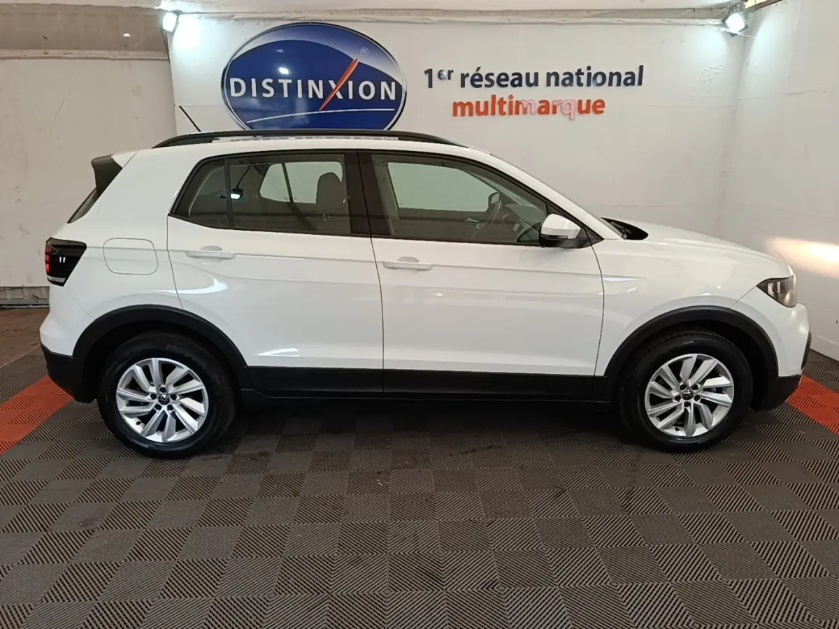 Vue de profil côté gauche d'un Volkswagen T-Cross blanc 2022 avec jantes alliage et barres de toit noires.