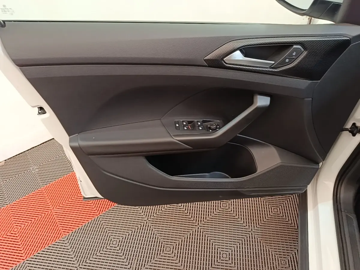 Vue de profil intérieur sur la porte avant gauche blanche du Volkswagen T-Cross avec commandes de vitres et poignée grise.
