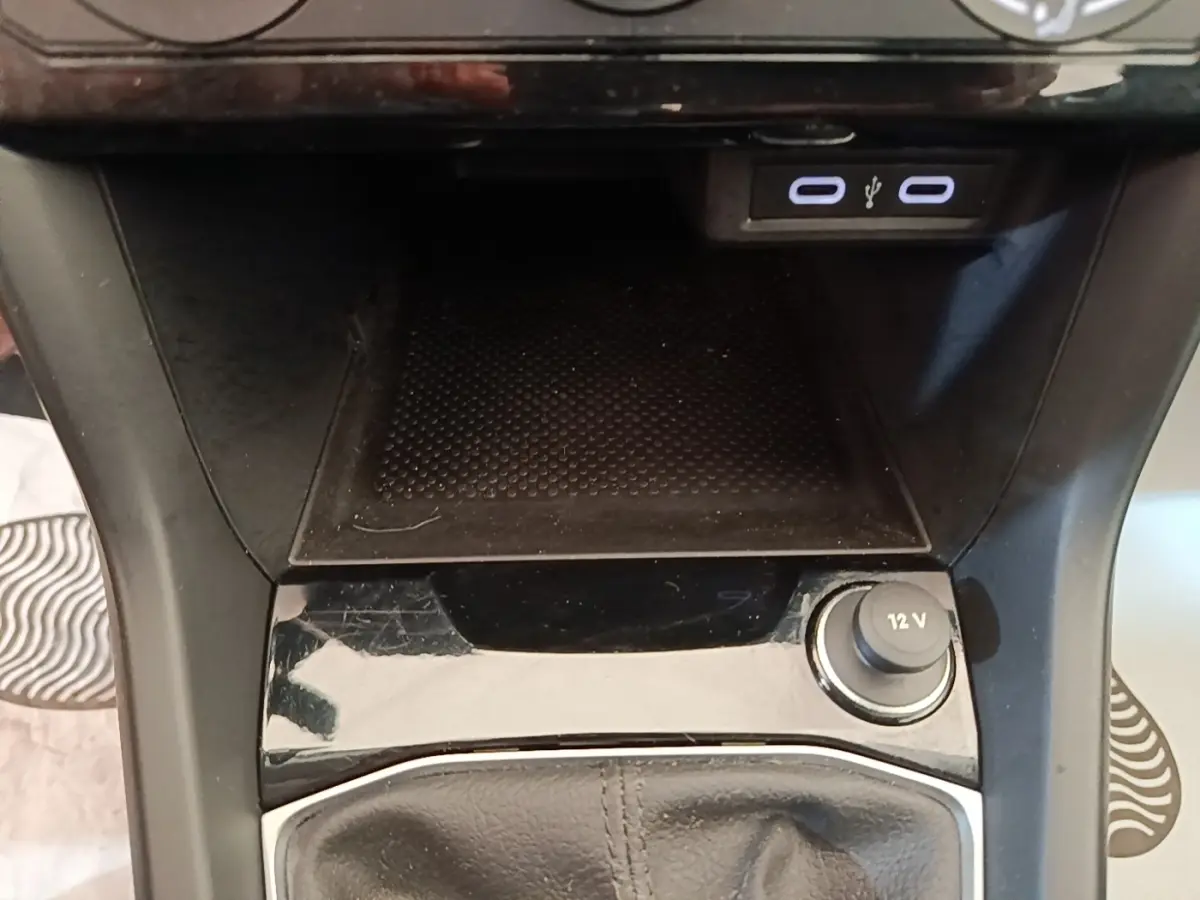 Gros plan sur la console centrale du Volkswagen T-Cross 2022, montrant les ports USB et la prise 12V avec finition noire brillante.