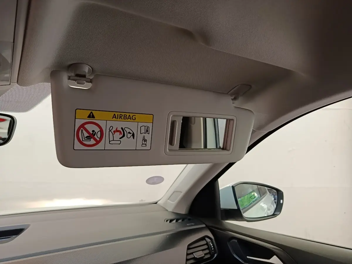Détail intérieur du pare-soleil côté conducteur avec miroir et avertissement airbag du Volkswagen T-Cross blanc.