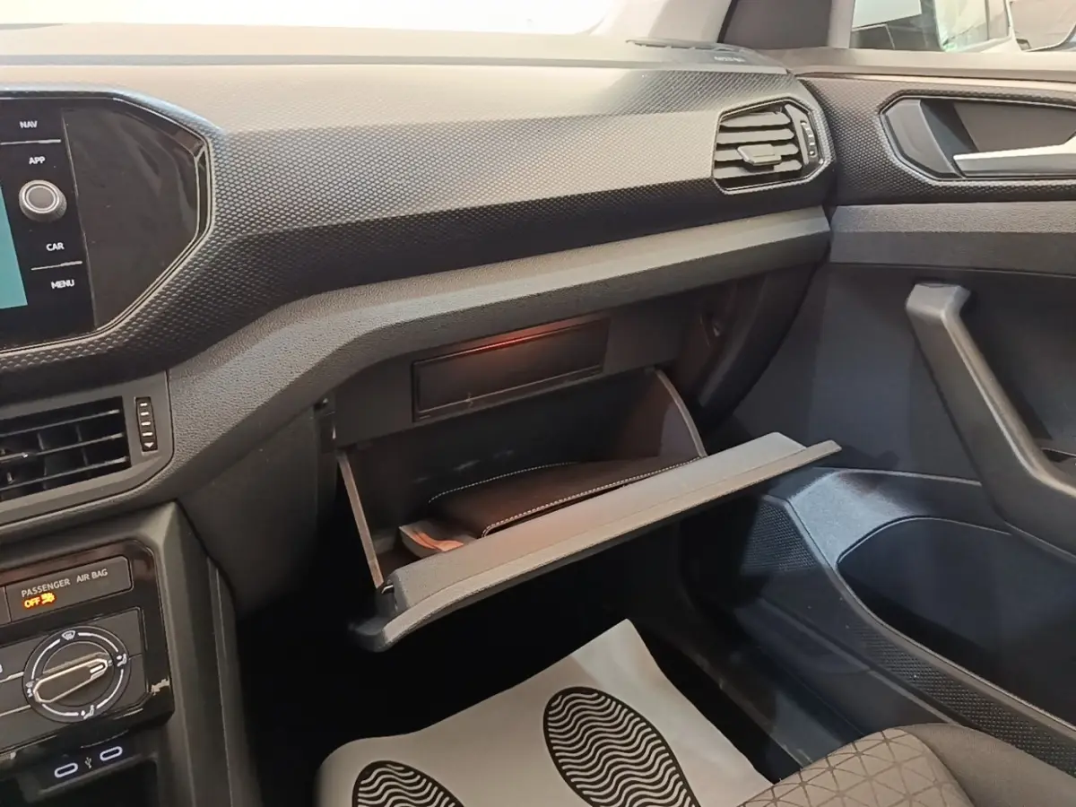 Intérieur du Volkswagen T-Cross 2022, vue côté passager avec boîte à gants ouverte et tableau de bord noir texturé.