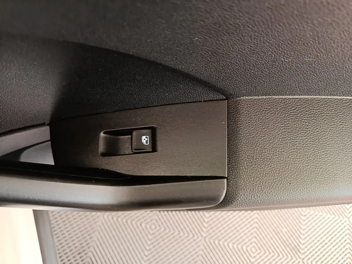 Gros plan sur le bouton de commande de lève-vitre côté porte intérieure d’un Volkswagen T-Cross blanc.