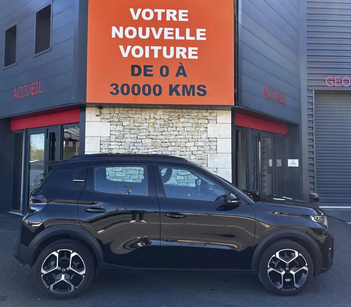Profil côté gauche d'une Citroën C3 Turbo 100 BVM6 MAX noire, garée devant un bâtiment avec panneau orange.