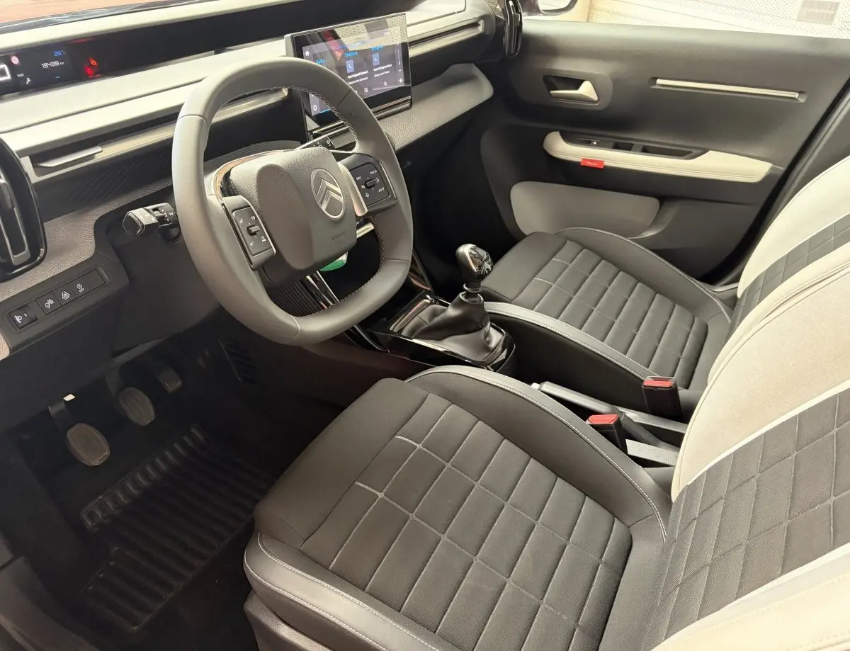 Vue intérieure côté conducteur de la Citroën C3 2025 noire, avec volant cuir, écran tactile et sièges bi-ton gris et beige.