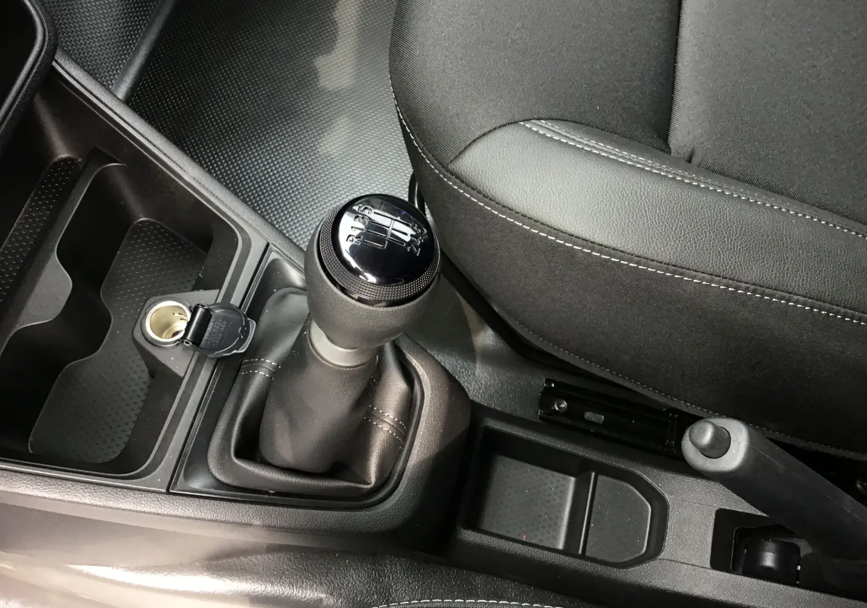 Gros plan intérieur sur le levier de vitesse manuel et la console centrale du Renault Express Van blanc, siège conducteur en tissu noir.