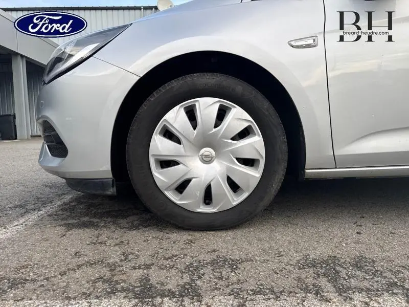 Gros plan sur la roue avant gauche d'une Opel Astra gris minéral avec enjoliveur et partie avant du véhicule visible.