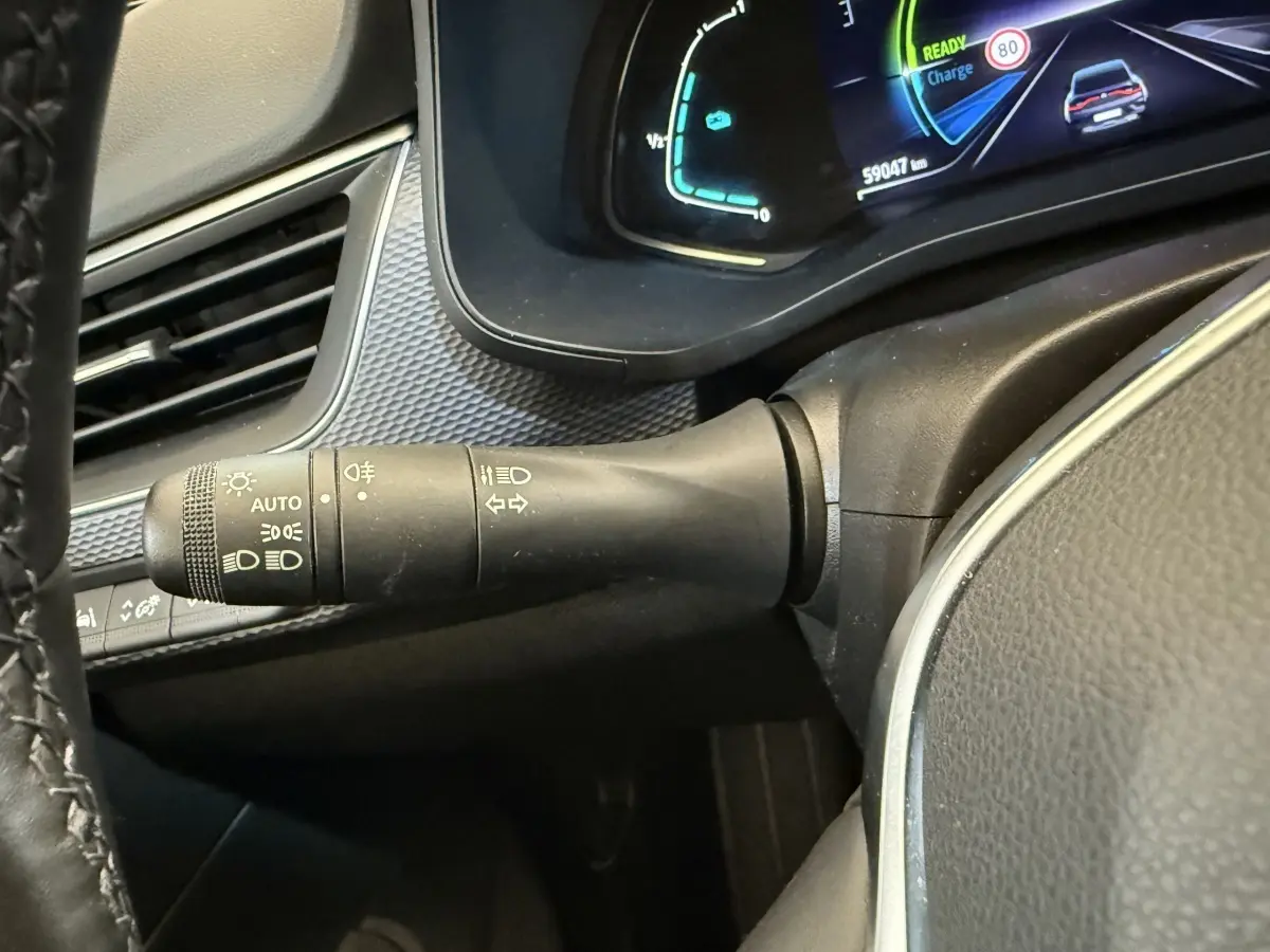 Gros plan sur la manette de commandes d’éclairage et clignotants, tableau de bord numérique bleu et noir visible côté gauche.