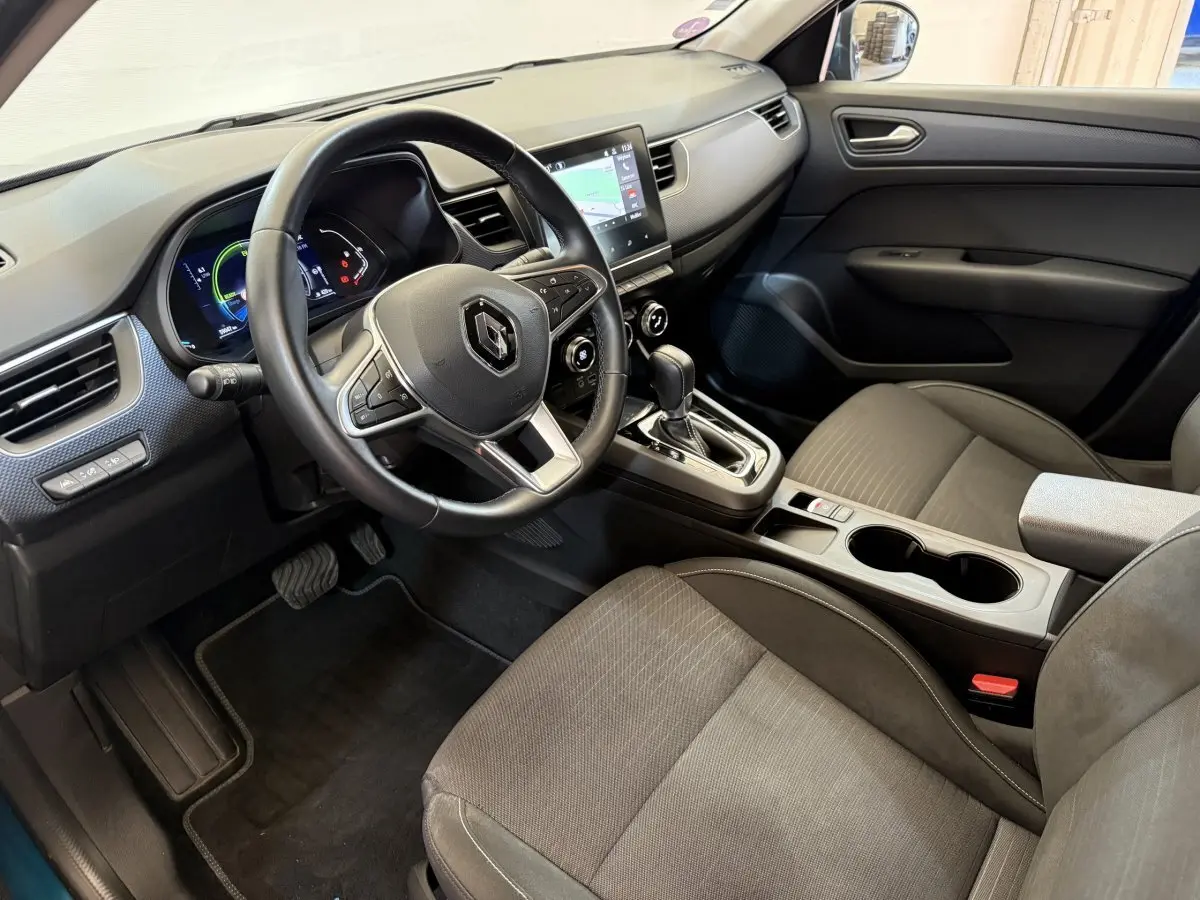 Vue intérieure côté conducteur de la Renault Arkana Business E-TECH 145 avec volant multifonctions et écran tactile central.