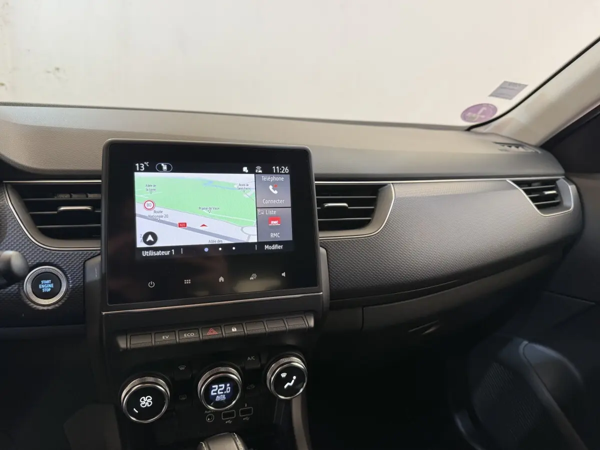 Vue intérieure du tableau de bord de la Renault Arkana Business E-TECH 145 avec écran tactile et commandes climatisation.