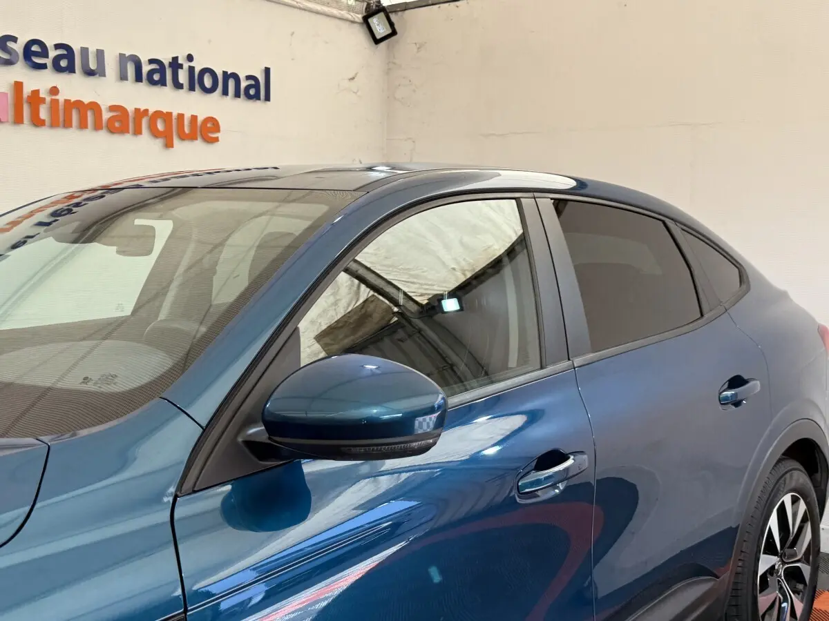 Vue de côté droit sur la partie avant d’une Renault Arkana Business E-TECH 145 bleu avec rétroviseur et poignées visibles.