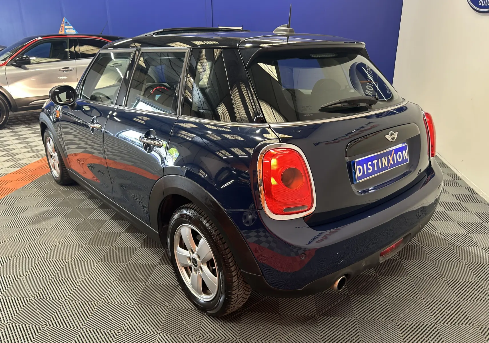 Vue 3/4 arrière droite d'une MINI 5 portes bleu foncé avec toit ouvrant, dans un showroom intérieur.