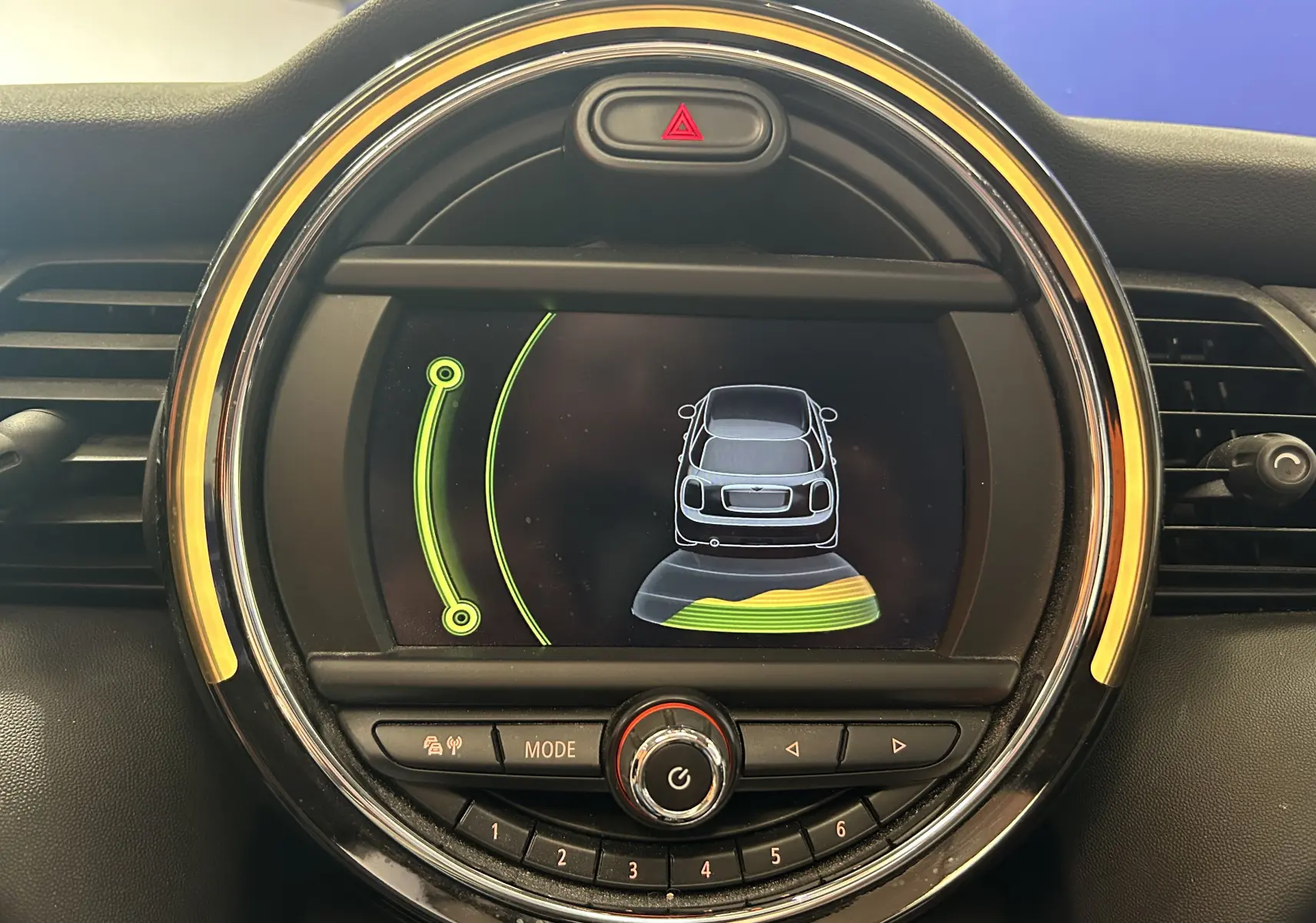 Affichage central du tableau de bord de la MINI 5P Cooper D 2015, montrant l'alerte de proximité arrière avec cercle lumineux jaune.