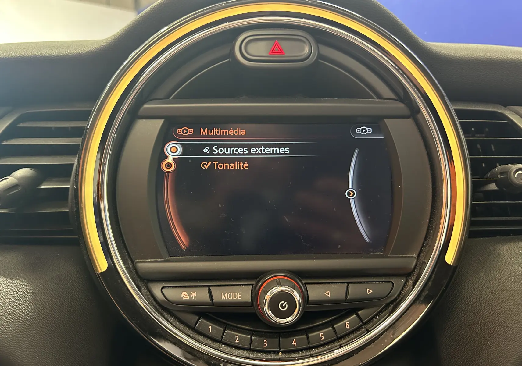 Gros plan sur l’écran multimédia circulaire du tableau de bord de la MINI 5P Cooper D 2015, entouré d’un anneau lumineux jaune.