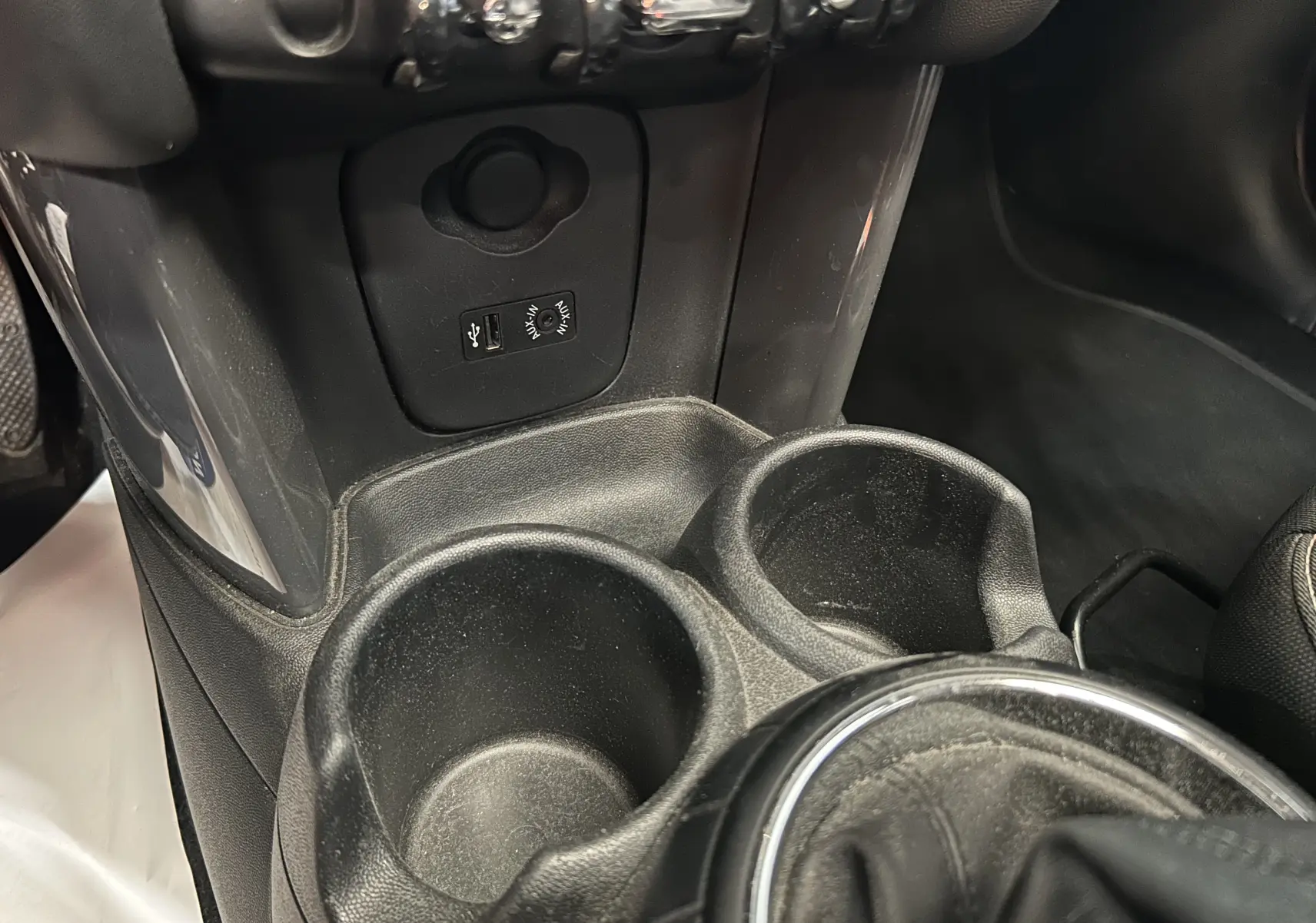 Gros plan sur la console centrale noire de la MINI 5P Cooper D 2015, montrant porte-gobelets et prises USB/AUX.