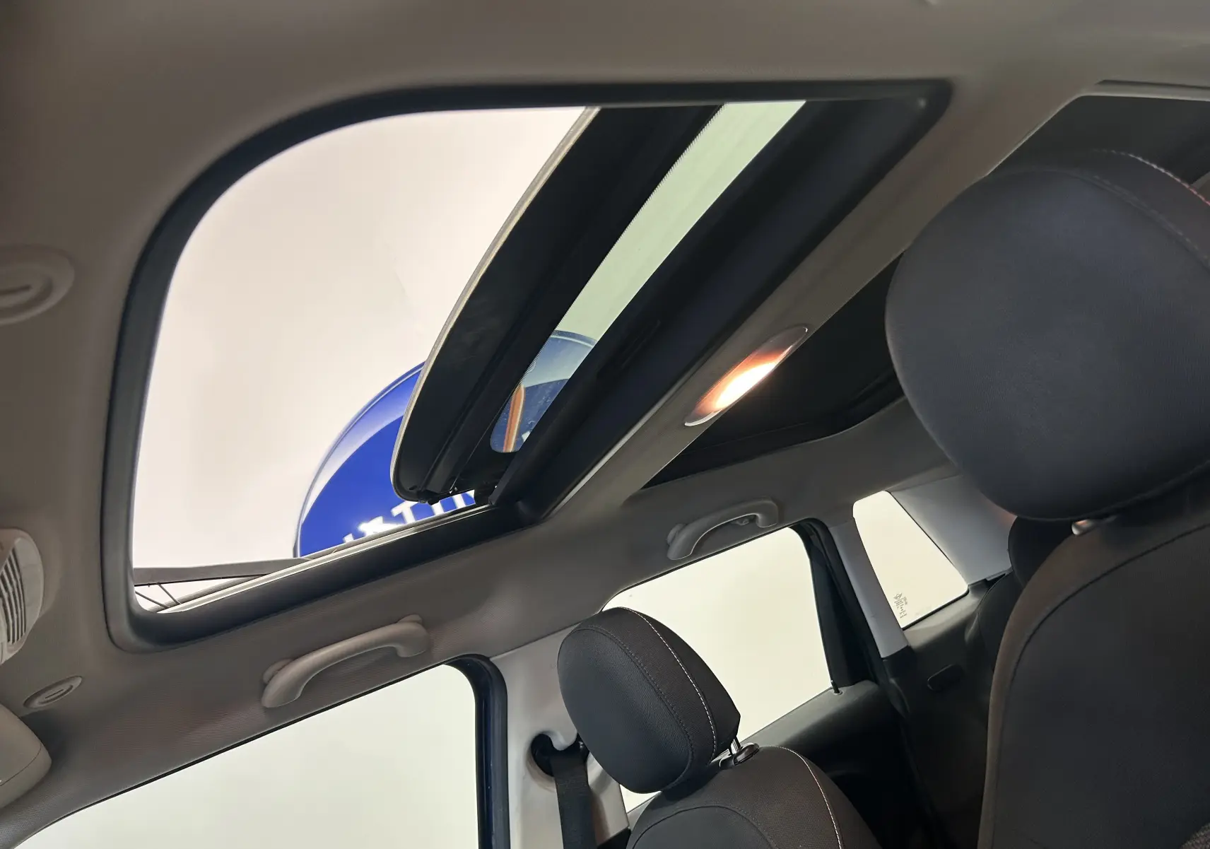 Vue intérieure du toit ouvrant panoramique ouvert sur la MINI 5 portes Cooper D bleu, avec sièges avant en tissu noir.