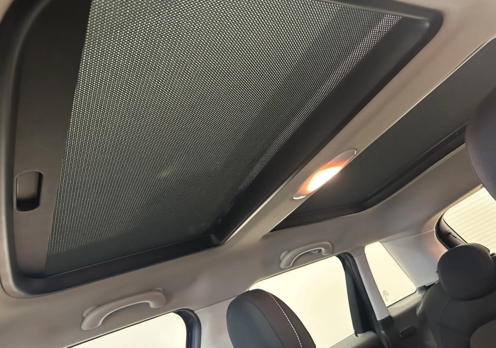 Vue intérieure du toit ouvrant avec pare-soleil déployé sur la MINI 5 portes bleu, éclairage intérieur allumé.