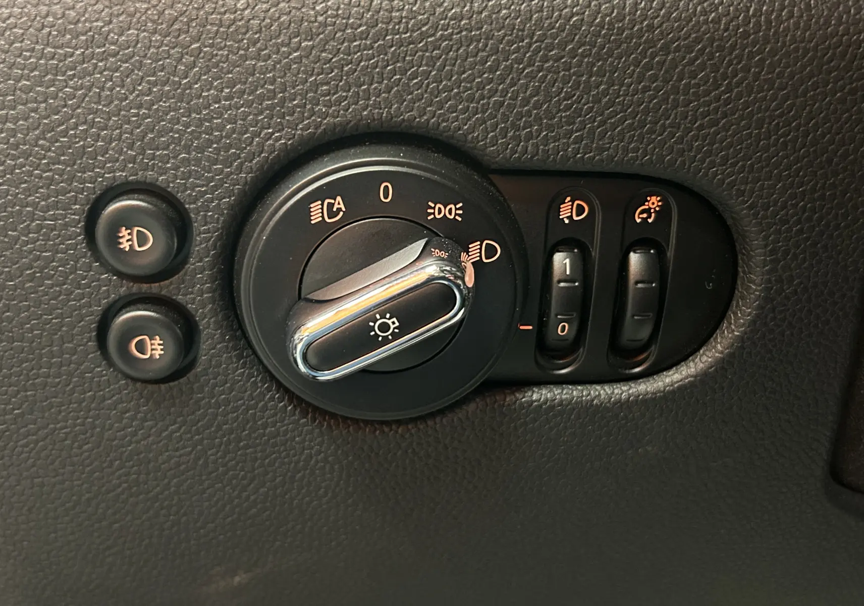 Gros plan sur la molette de réglage des phares et boutons de feux antibrouillard d'une MINI 5P bleu de 2015.
