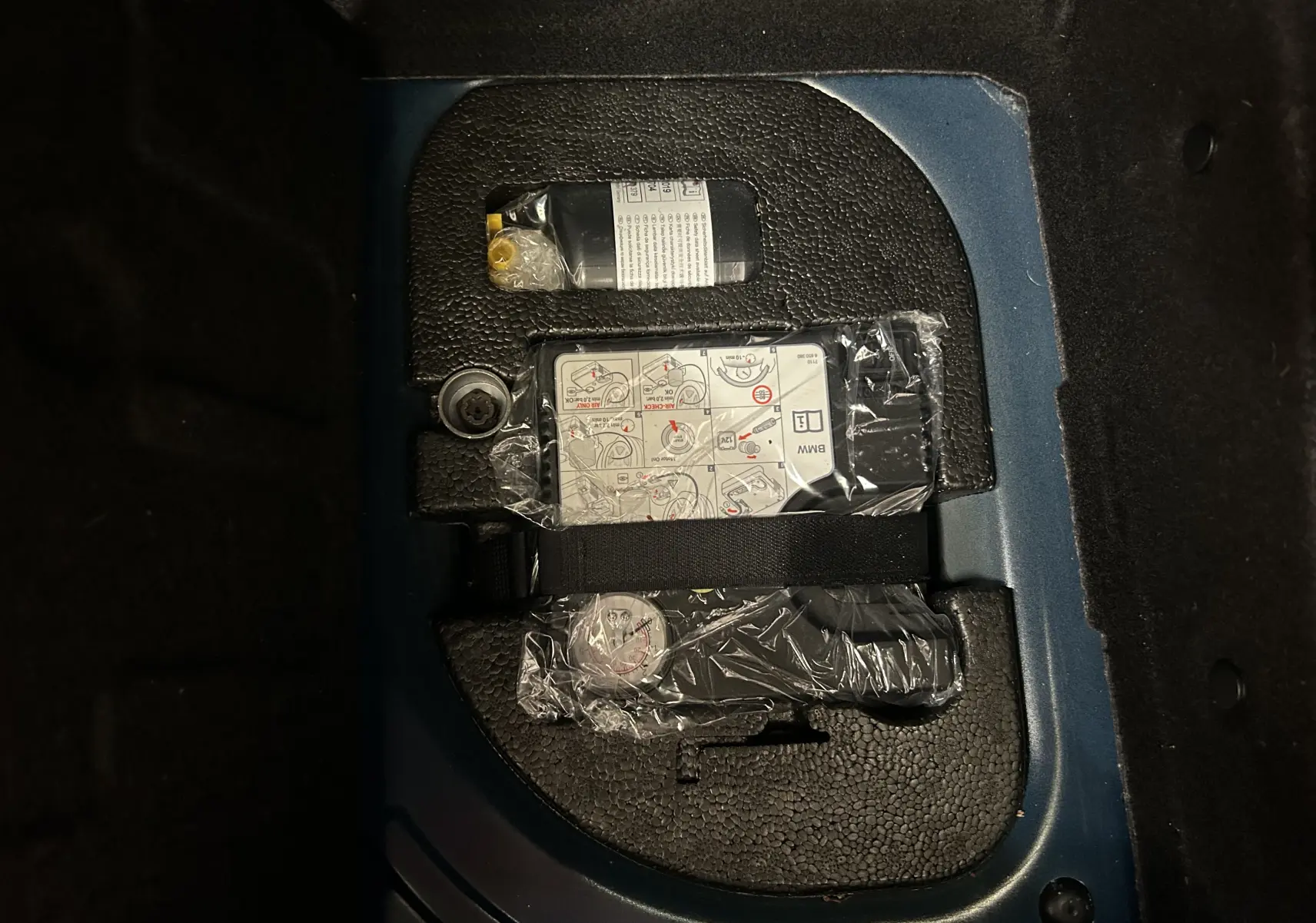Gros plan sur le coffre d’une MINI 5P Cooper D bleu, montrant le kit de réparation pneu rangé dans un compartiment.