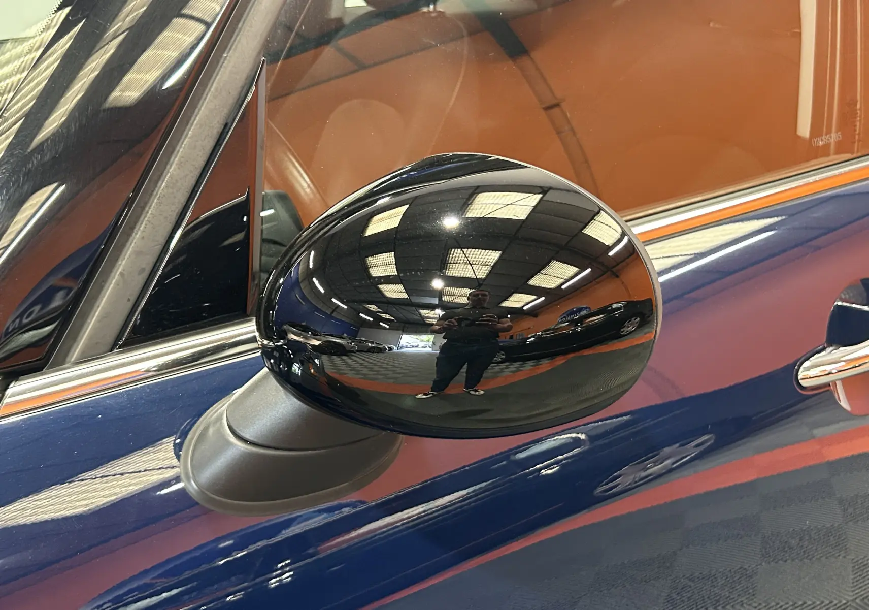 Gros plan sur le rétroviseur extérieur noir côté gauche d'une MINI 5P Cooper D bleu, avec reflet intérieur cuir marron.