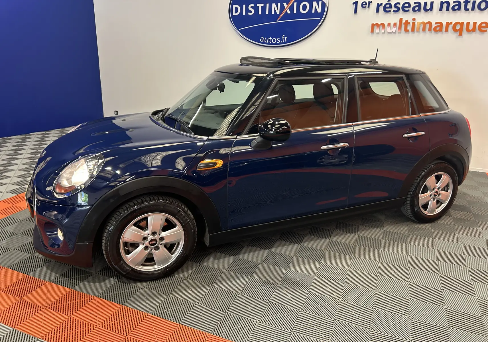 Vue latérale droite d'une MINI 5 portes Cooper D bleu avec toit ouvrant et jantes alliage, stationnée en intérieur.