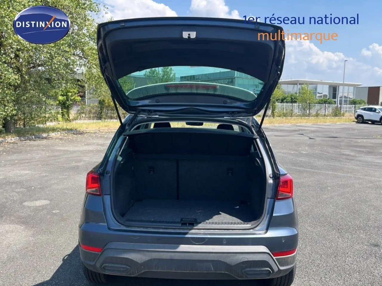 Vue arrière d'un SEAT Arona gris Magnetic avec coffre ouvert, toit blanc visible sous un ciel bleu.