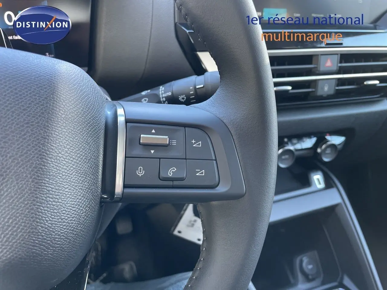 Gros plan sur les commandes au volant côté gauche d'une Citroën C4 hybride 2026, intérieur noir moderne.