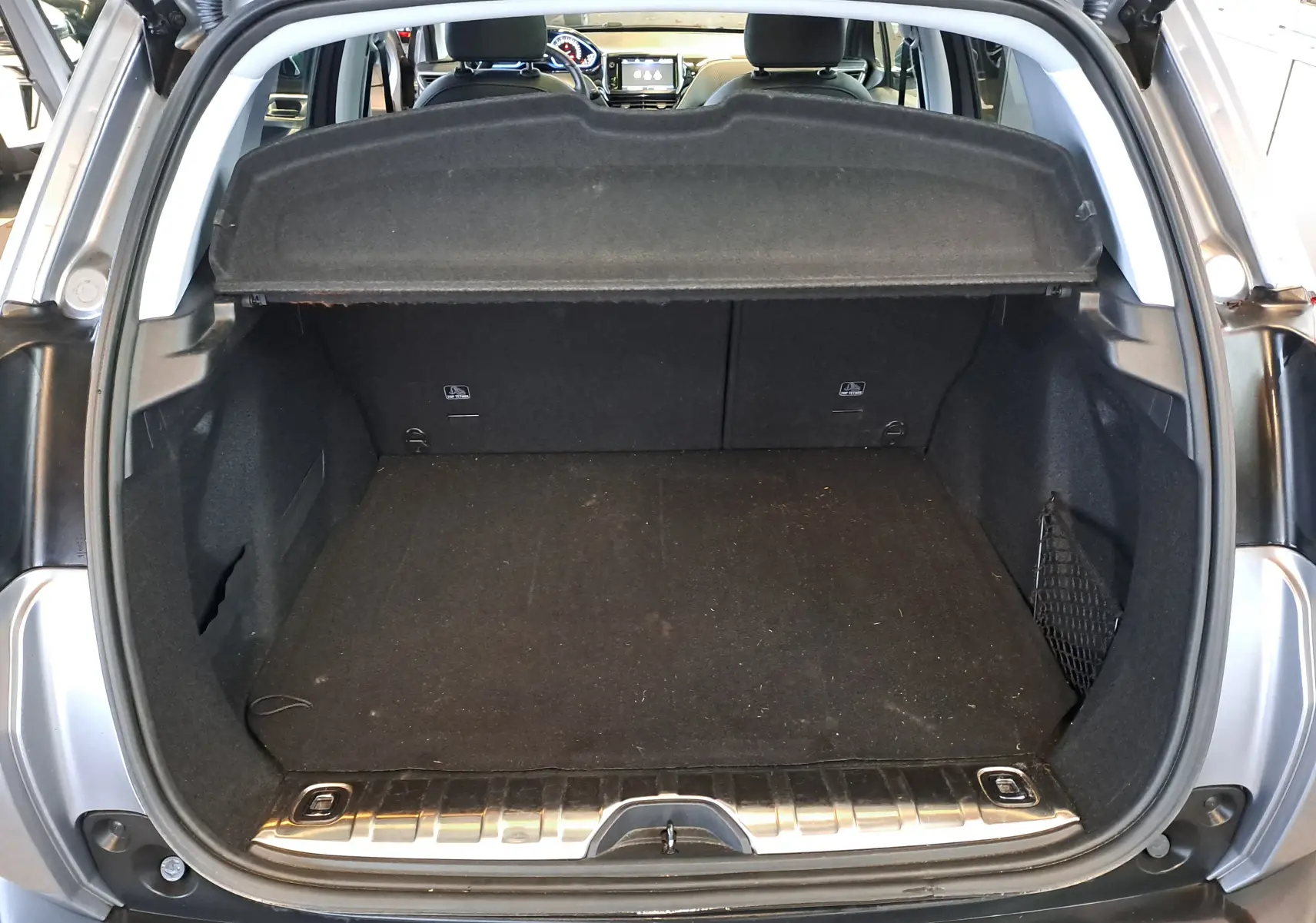 Coffre ouvert vu de l'arrière d'un Peugeot 2008 gris 2019, montrant un espace de chargement propre et une tablette cache-bagages.