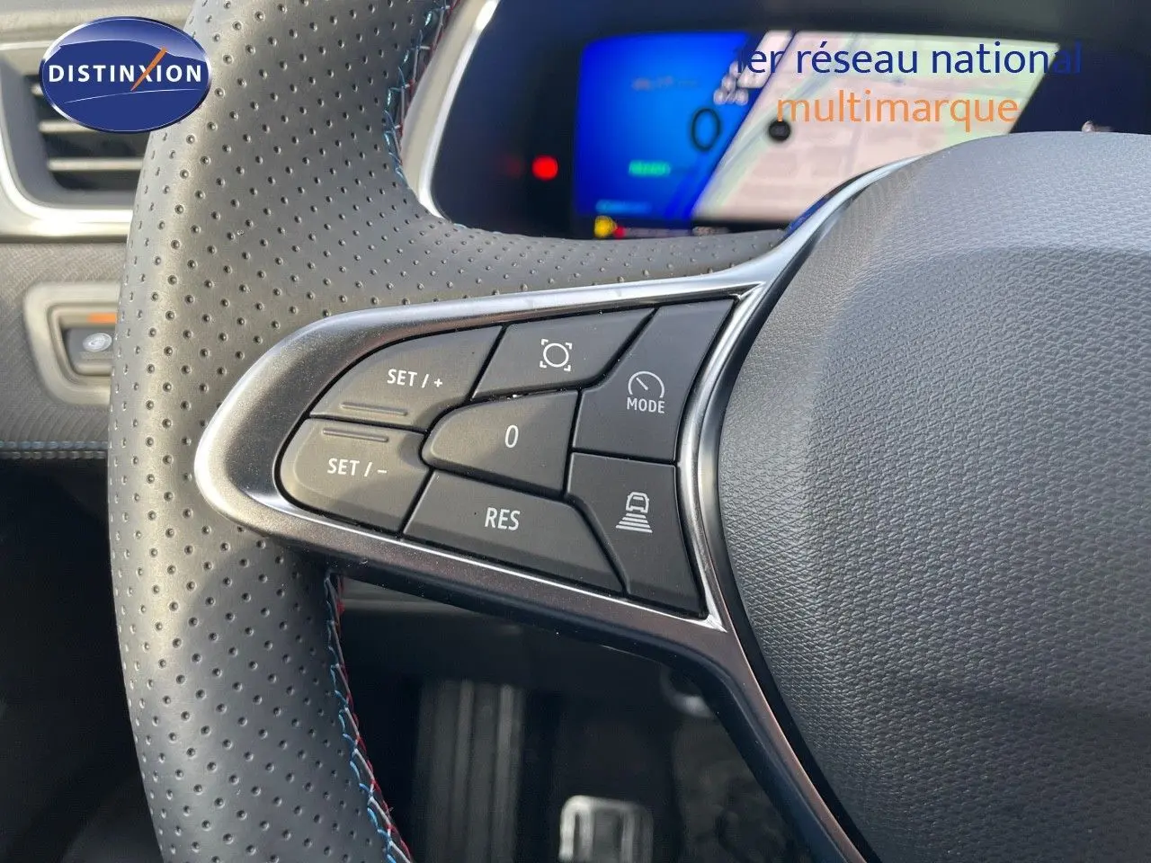 Gros plan sur le volant perforé avec commandes intégrées du Renault Symbioz gris Rafale, tableau de bord numérique en arrière-plan.