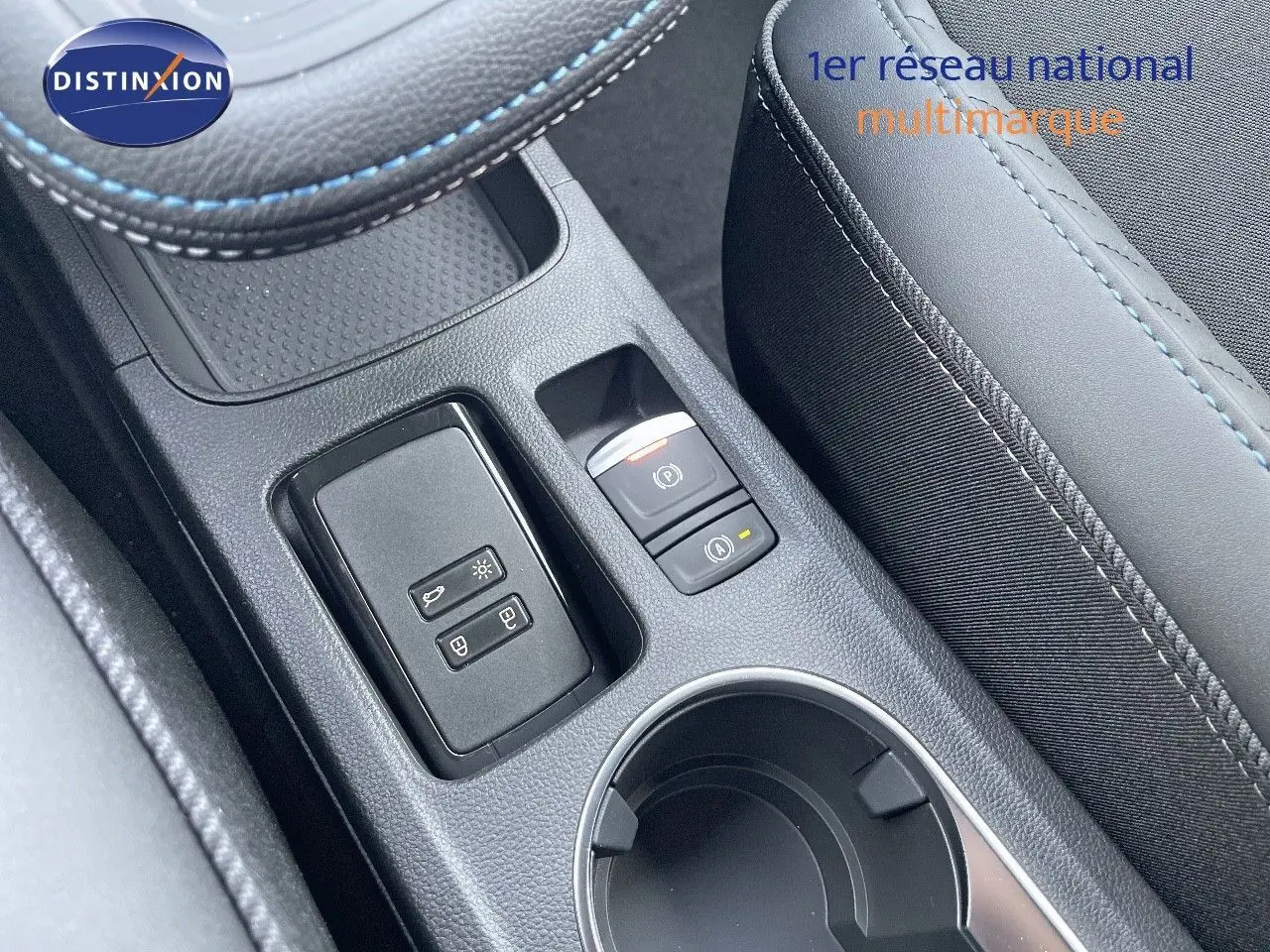 Gros plan sur la console centrale du Renault Symbioz gris Rafale, avec boutons de frein à main et porte-gobelet visible.