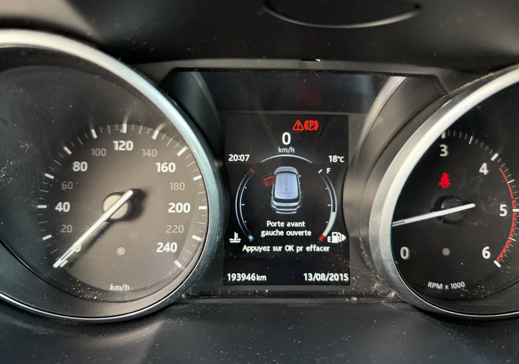 Tableau de bord du Range Rover Evoque gris montrant la vitesse, le compte-tours et l'alerte porte avant gauche ouverte.