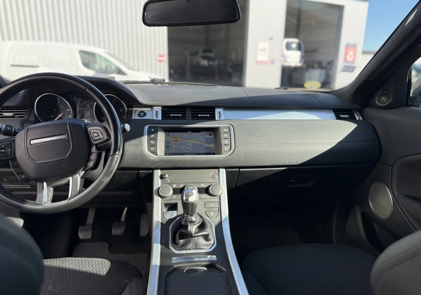 Vue intérieure avant du Range Rover Evoque gris, montrant le tableau de bord avec écran tactile et volant multifonction.