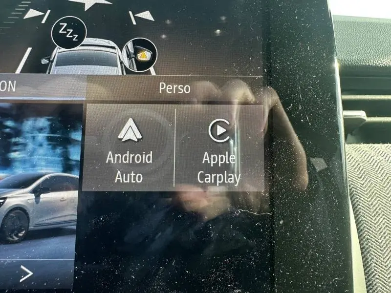 Écran tactile intérieur de la Renault Clio 2025 montrant les options Android Auto et Apple Carplay, avec reflet et poussière visible.