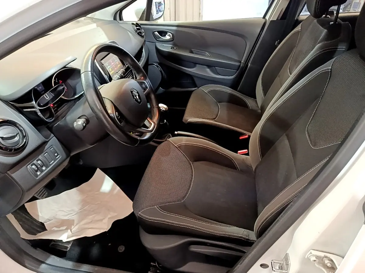 Vue intérieure côté conducteur de la Renault Clio Zen Energy dCi 75 blanche, volant cuir et sièges noirs avec coutures contrastées.