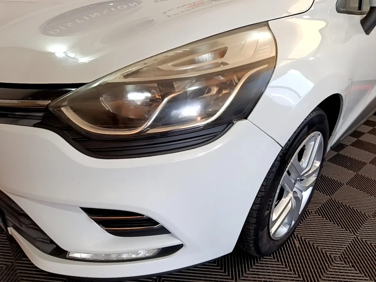 Gros plan sur l'avant droit blanc d'une Renault Clio 2016, mettant en valeur le phare et la roue alliage.