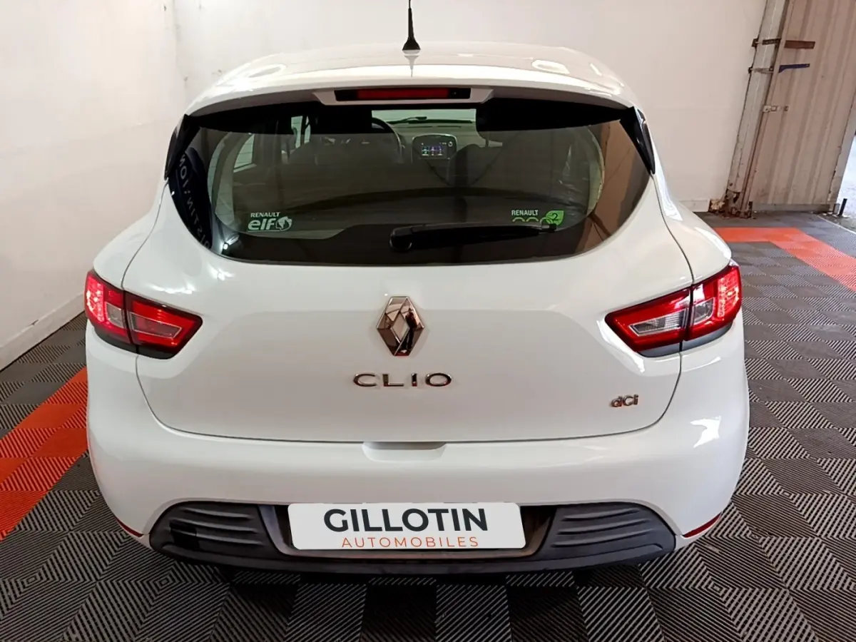 Vue arrière d'une Renault Clio Zen Energy dCi blanche de 2016 avec feux arrière allumés et logo visible.