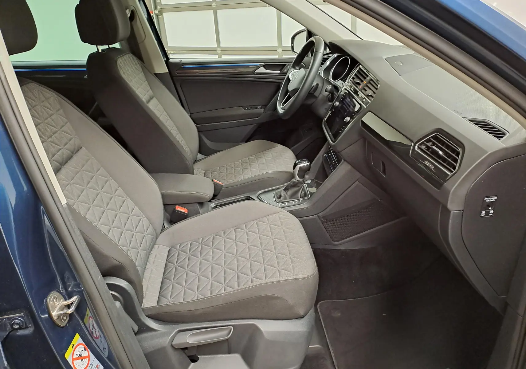 Vue intérieure côté conducteur du Volkswagen Tiguan 2023 avec sièges tissu gris et détails de la planche de bord.