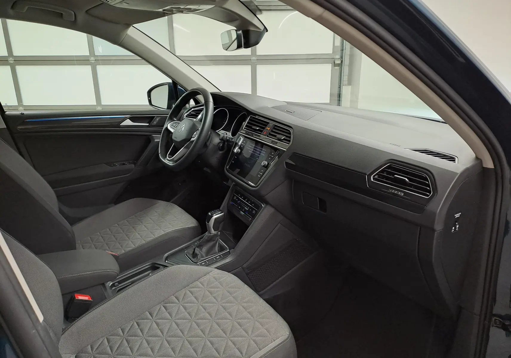 Vue intérieure côté conducteur du Volkswagen Tiguan 2023 Nightshade Blue, avec tableau de bord moderne et sièges gris à motifs.