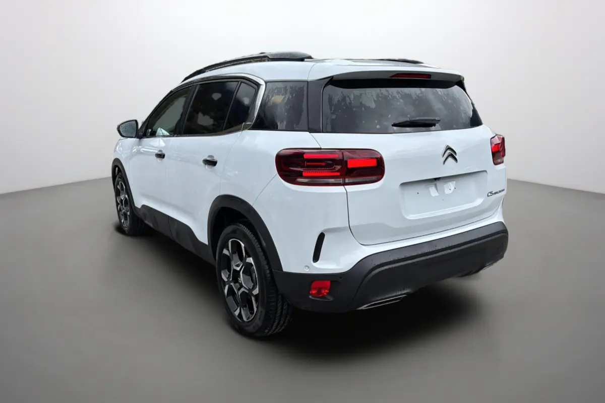 Vue 3/4 arrière droite d'un Citroën C5 Aircross Hybrid blanc okénite avec barres de toit et vitres surteintées.