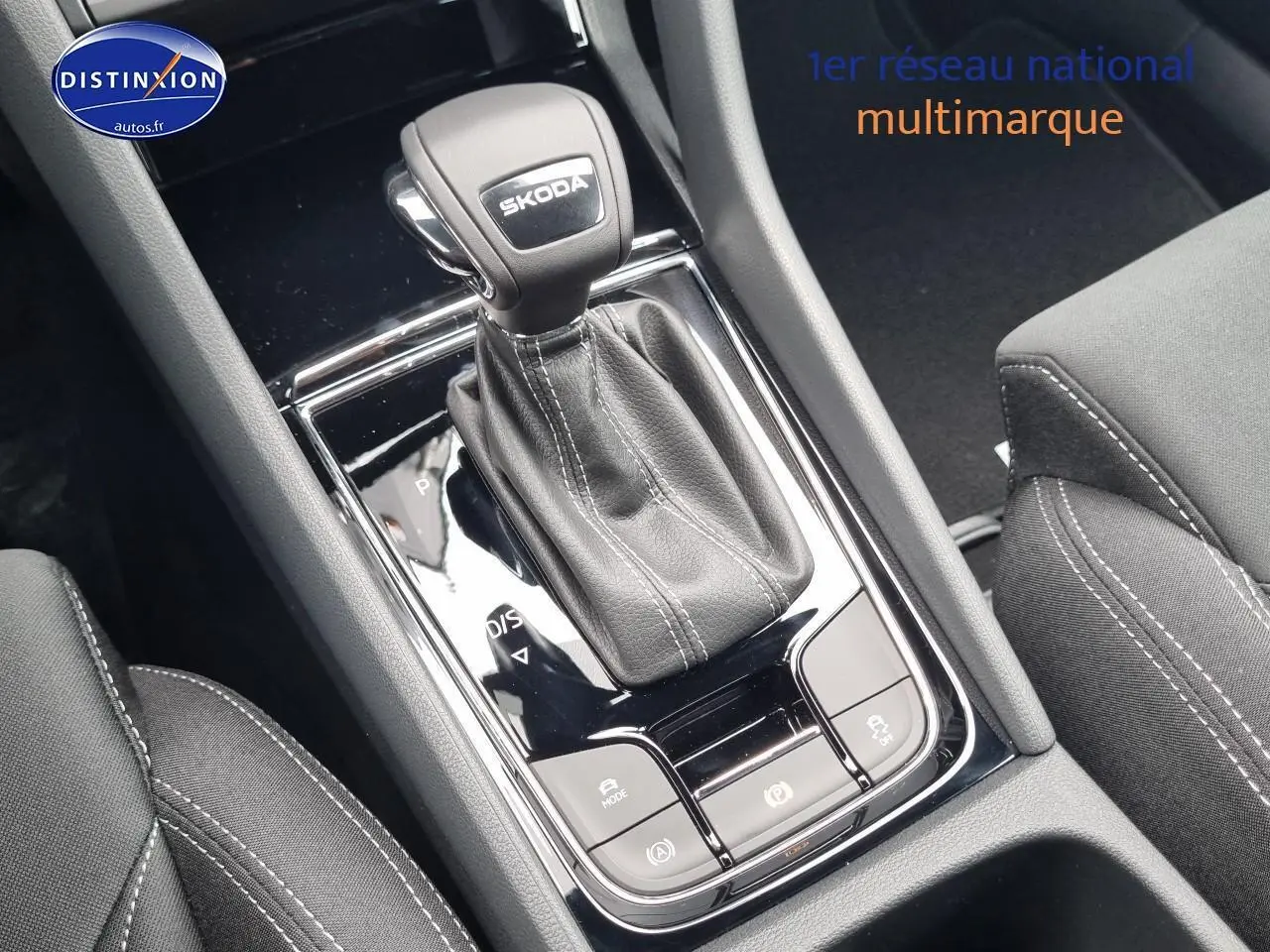 Gros plan sur la console centrale noire du Skoda Karoq 2025, avec levier de vitesse automatique et coutures blanches visibles.