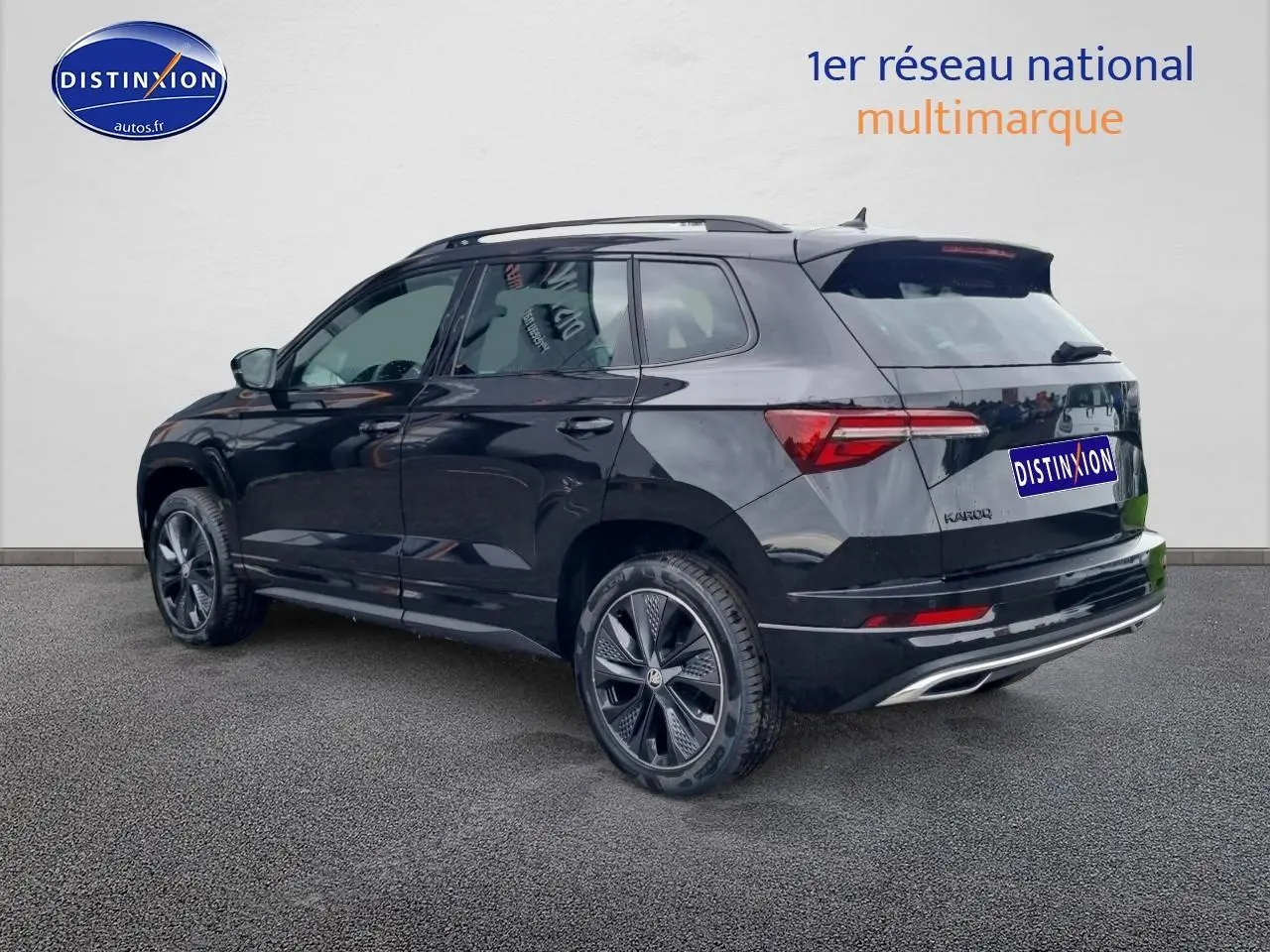 Vue 3/4 arrière droite d’un Skoda Karoq noir 2025 avec jantes alu noires et barres de toit visibles.